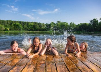 Happy Little Girls Having Fun Playing In A Lake Splashing Water During Summer Swedish Coolcation