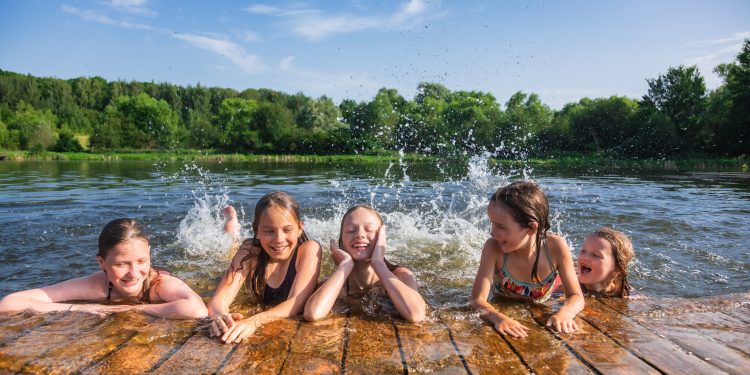 Happy Little Girls Having Fun Playing In A Lake Splashing Water During Summer Swedish Coolcation